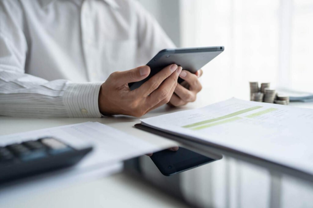 יד מחזיקה טלפון חכם עם מחשבון פתוח מעל מסמכי תביעה ופיצויים בגין אובדן כושר עבודה.